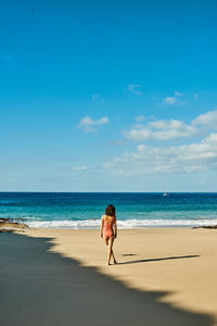 Rear view of woman walking at beach against sky