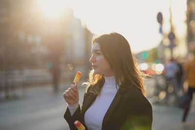 Thoughtful beautiful woman holding flavored ice in city