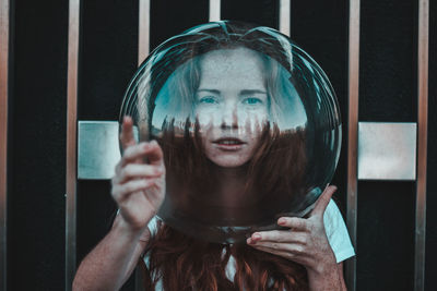 Close-up portrait of young woman gesturing while wearing glass helmet in head against metallic railing