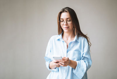 Portrait of young smiling woman with dark long hair in blue shirt using mobile phone in hand