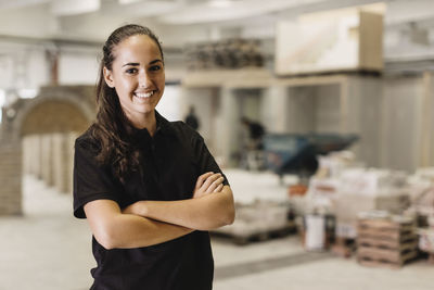 Portrait of happy female carpentry student standing arms crossed at workshop