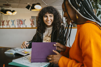 Smiling young woman looking at friend while studying together in university cafeteria