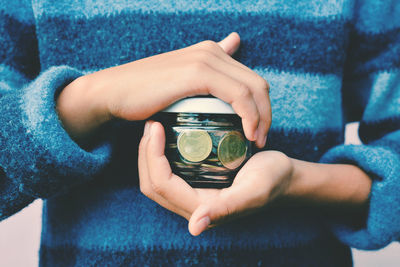 Midsection of woman holding coins in container