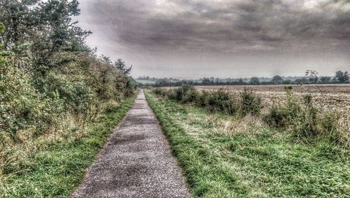 Road passing through field against cloudy sky