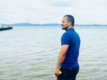 Young man looking at sea against sky