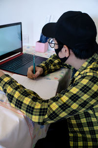 Young boy taking classes using laptop, using cell phone, writing notes and smiling, online classes