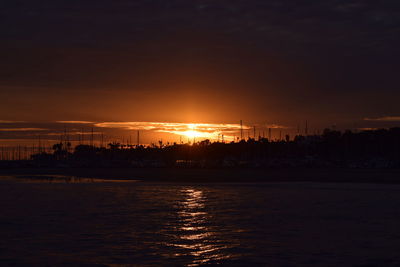 Silhouette of city at waterfront during sunset