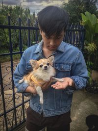 Man holding chihuahua by metallic fence