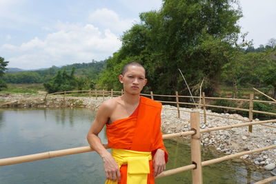 Young man standing by railing against trees