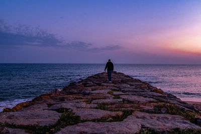 People standing on rock by sea against sky during sunset