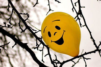 Low angle view of yellow balloon with human face on amidst bare tree branches