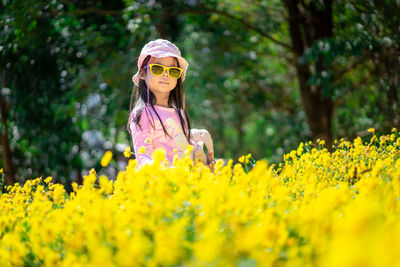 Portrait of girl standing by yellow flowers on field
