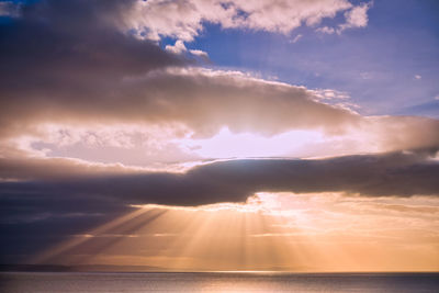 Sunlight streaming through clouds over sea during sunset