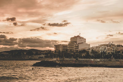 Scenic view of sea by buildings against sky during sunset