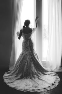 Rear view of woman standing by window at home