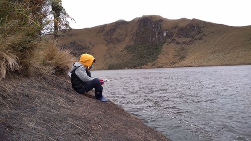 Side view of boy fishing in on lake by mountain