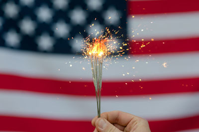 Cropped hand holding sparkler against american flag