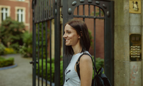 Side view of smiling woman looking away while standing by gate