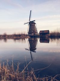 Traditional windmill by lake against sky