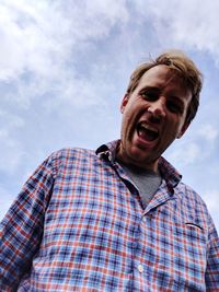 Low angle portrait of man screaming against sky
