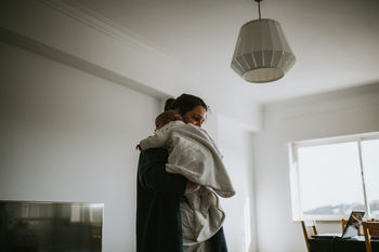 Side view of mother carrying daughter while standing against wall at home