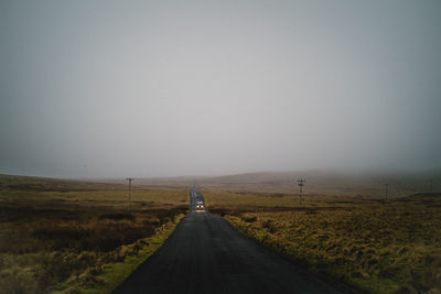 Road amidst field against clear sky