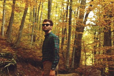 Portrait of young man standing by trees in forest