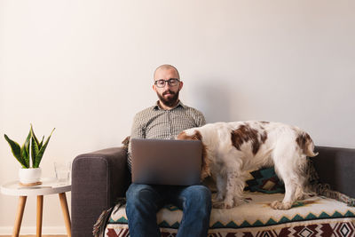 Man using laptop by dog while sitting on sofa
