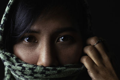 Close-up portrait of young woman covered with scarf against black background