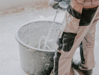 A young caucasian guy a plasterer holds a construction electric mixer and stirs dry putty with water