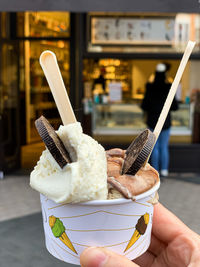 Womans hand is holding cup with two ice cream scoops. vanilla and hazelnut ice cream with chocolate