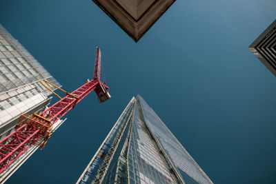 Low angle view of crane and buildings against clear blue sky