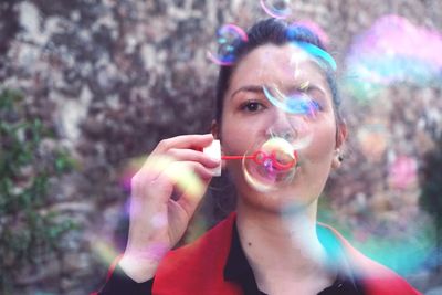 Close-up of young woman blowing bubbles against wall