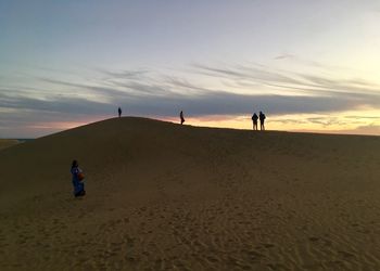 People on beach against sky during sunset