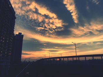 Silhouette buildings by street against sky during sunset