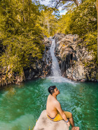 Young man sitting on rock by waterfall