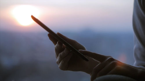 Close-up of hand holding umbrella against sky during sunset