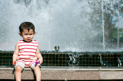 Cute girl sitting against water fountain