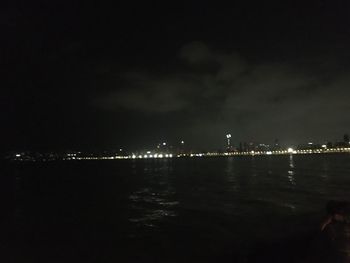 Illuminated buildings by sea against sky at night