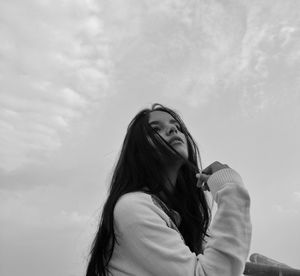 Beautiful young woman looking away while sitting against sky