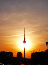 Silhouette fernsehturm in city against orange sky