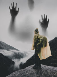 Digital composite image of hiker on mountain with hands in sky