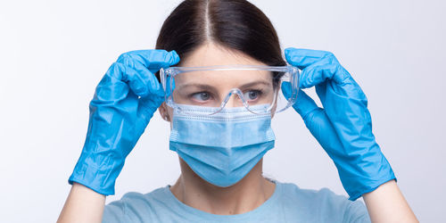 Doctor in mask wearing surgical glove looking away against gray background