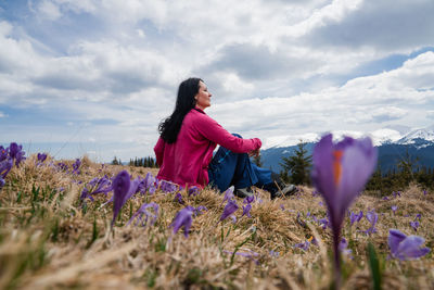 Rear view of woman standing amidst purple flowering plants on field against sky