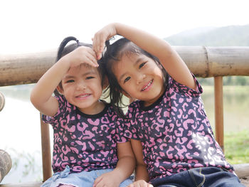 Portrait of smiling sisters against lake at park