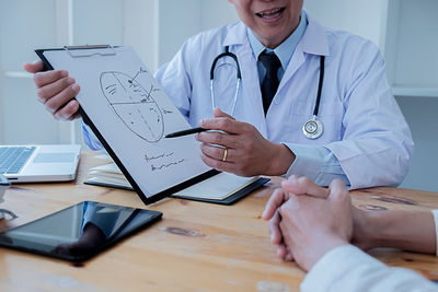 Midsection of man holding smart phone on table