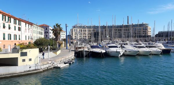 Sailboats moored on harbor by buildings in city against sky