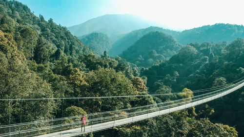 Scenic view of mountains with man standing on footbridge against sky