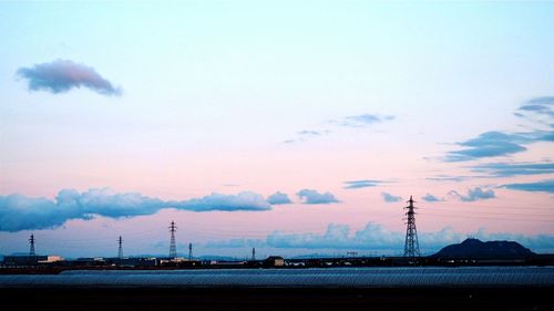 Electricity pylons against sky during sunset