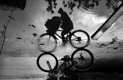 Silhouette of man with bicycle in puddle